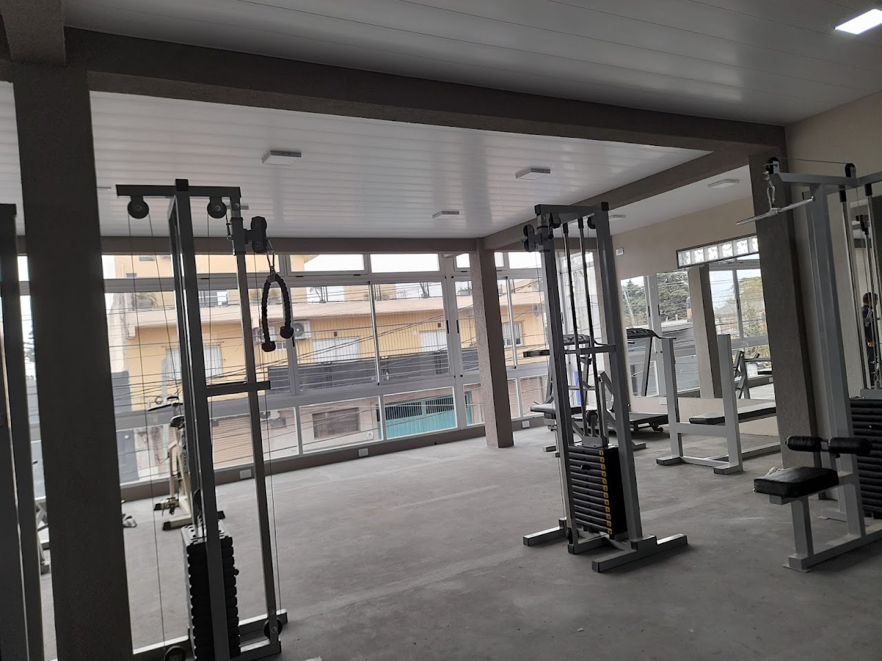 Modern gym cardio and functional training zone, high end treadmills, rowers, assault bikes in a clean spacious dark gym with warm orange architectural backlights and industrial ceiling